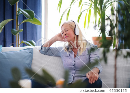 Attractive senior woman with headphones sitting indoors on sofa, relaxing. Attractive senior woman with headphones sitting indoors on sofa, relaxing. 65330155