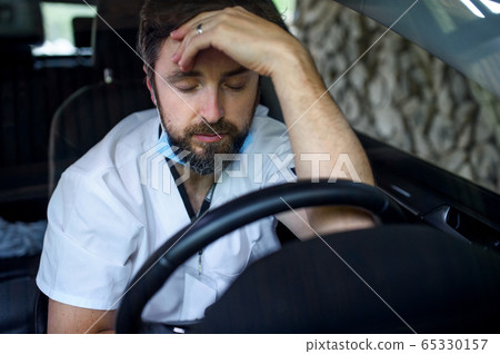 Tired and exhausted doctor sitting in car after long and difficult shift. Tired and exhausted doctor sitting in car after long and difficult shift. 65330157