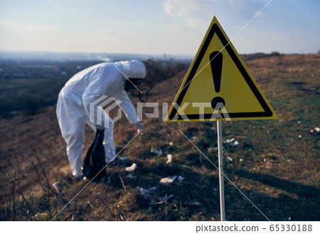 Environmentalist picking up trash in field with warning sign. Environmentalist picking up trash in field with warning sign. 65330188