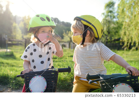 Small children with face masks playing outdoors with bike, coronavirus concept. 65330213