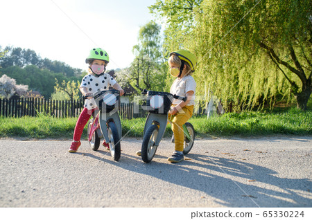 Small children with face masks playing outdoors with bike, coronavirus concept. Small children with face masks playing outdoors with bike, coronavirus concept. 65330224