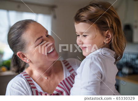 Small girl with senior grandmother in kitchen indoors at home. Small girl with senior grandmother in kitchen indoors at home. 65330329