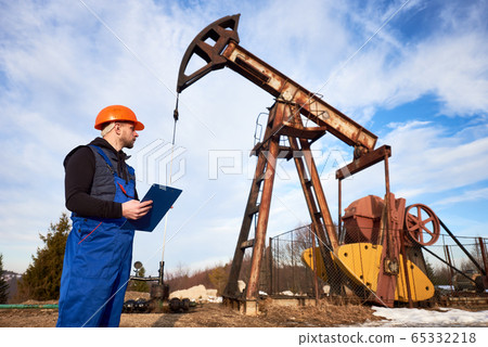 Oil man checking work of oil well pump jack. Oil man checking work of oil well pump jack. 65332218