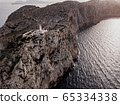 Aerial view on beautiful white Lighthouse of Cap de Formentor in the Coast of North Mallorca, Spain Balearic Islands at sunset. Wide view of wild rocky cliffs. Serpentine Road 65334338