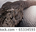 Aerial view on beautiful white Lighthouse of Cap de Formentor in the Coast of North Mallorca, Spain Balearic Islands at sunset. Wide view of wild rocky cliffs. Serpentine Road 65334593