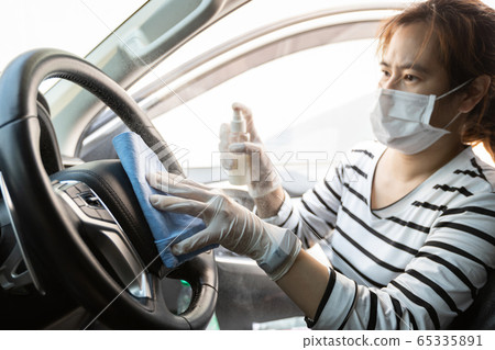 Woman wear protective glove,spraying alcohol antiseptic,disinfecting spray,cleaning on steering wheel in car,prevent infection of Covid-19,Coronavirus,wipe clean surfaces that are frequently touched 65335891