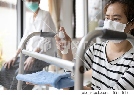 Caregiver in a mask,using spraying alcohol antiseptic,disinfecting spray,cleaning on walking aids,walker for the senior,during Coronavirus pandemic,Covid-19,wipe clean the elderly equipment at home 65336153