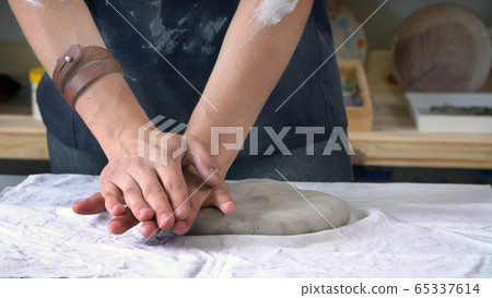 Female sculptor's hands are kneading clay for a ceramic plate Female sculptor's hands are kneading clay for a ceramic plate 65337614