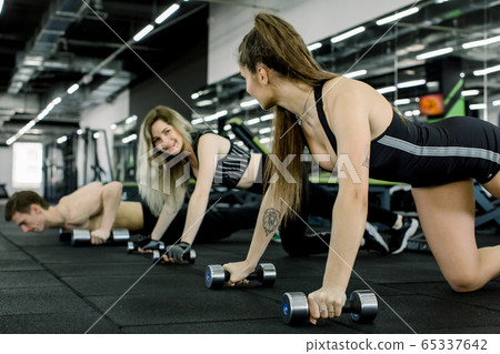 Portrait of young fitness people doing pushing up exercise with dumbbell in gym. People lifestyle and Sport concept. Three friends holding weight by two hands on floor. 65337642