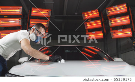 man in glasses and a mask, a respirator polishes the car with a sponge and a special chemical composition to protect the paint on the body from scratches man in glasses and a mask, a respirator polishes the car with a sponge and a special chemical composition to protect the paint on the body from scratches 65339175
