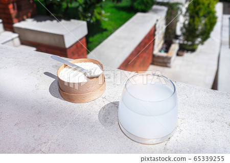 Collagen with a spoon and glass of water on concrete background. Collagen with a spoon and glass of water on concrete background. 65339255