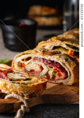 Traditional Italian Stromboli stuffed with cheese, salami, red pepper and spinach. Photo in a dark style. 65339590