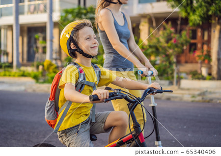 Active school kid boy and his mom in safety helmet riding a bike with backpack on sunny day. Happy 65340406