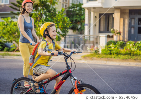 Active school kid boy and his mom in safety helmet riding a bike with backpack on sunny day. Happy 65340456