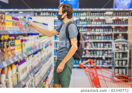 Alarmed man wears medical mask against coronavirus while purchase of household chemicals in 65340772