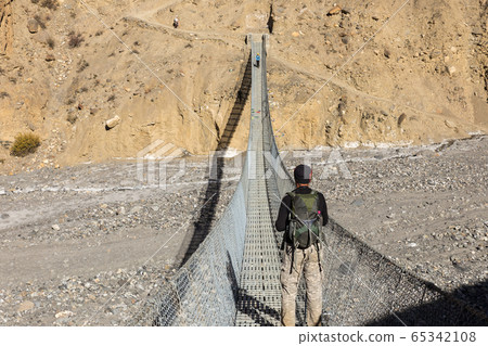 A man with a backpack stands on a suspension bridge. A man with a backpack stands on a suspension bridge. 65342108