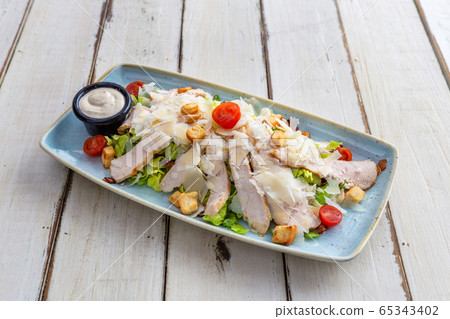 Salad of thinly sliced meat with tomatoes, lettuce and vegetables. White plate on a wooden table. Close-up. Salad of thinly sliced meat with tomatoes, lettuce and vegetables. White plate on a wooden table. Close-up. 65343402