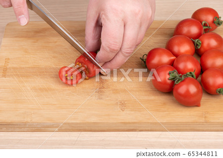 Slicing cherry tomatoes on a cutting board. 65344811