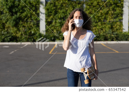 Caucasian woman wearing a protective mask in the streets and using her phone 65347542