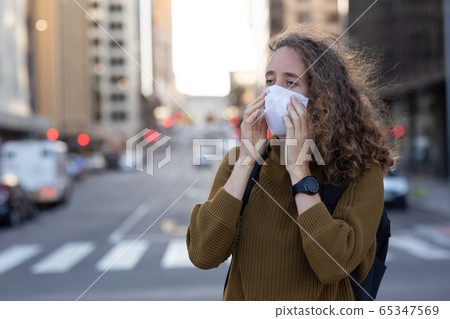 Caucasian woman putting on a protective mask in the streets 65347569