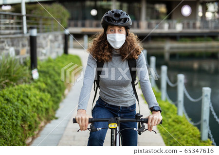 Caucasian woman wearing a protective mask and a cycling helmet in the streets, biking in the streets 65347616