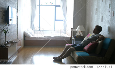 Handsome Young Man at Home Sitting on a Couch Watches TV, Laughs at Comedy. Handsome Young Man at Home Sitting on a Couch Watches TV, Laughs at Comedy. 65351951