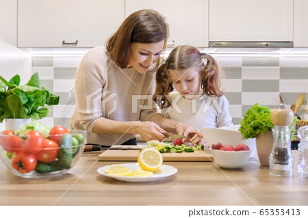 Mother and child cooking together at home in kitchen. Healthy eating, mother teaches daughter to cook Mother and child cooking together at home in kitchen. Healthy eating, mother teaches daughter to cook 65353413