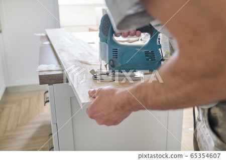 Close-up of carpenters hand using professional woodworking electric tools when working with wood. Male carving hole in wooden panel board, carpentry, woodwork, profession, people Close-up of carpenters hand using professional woodworking electric tools when working with wood. Male carving hole in wooden panel board, carpentry, woodwork, profession, people 65354607