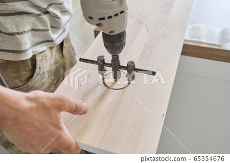Close-up of carpenters hand using professional woodworking electric tools when working with wood. Male carving hole in wooden panel board, carpentry, woodwork, profession, people 65354676