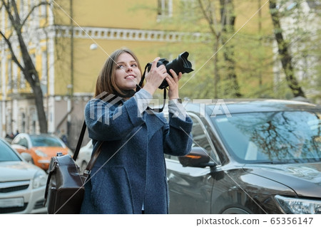 Beautiful young woman with camera in city. Tourist girl traveling and photographing, spring city street background Beautiful young woman with camera in city. Tourist girl traveling and photographing, spring city street background 65356147