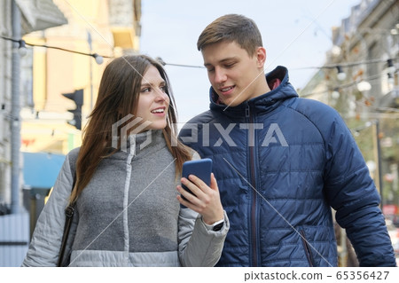 Young talking man and woman walking in city, looking into smartphone Young talking man and woman walking in city, looking into smartphone 65356427