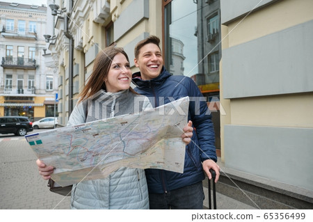 Outdoor portrait of young couple travelers in spring city, young man and woman reading city map Outdoor portrait of young couple travelers in spring city, young man and woman reading city map 65356499