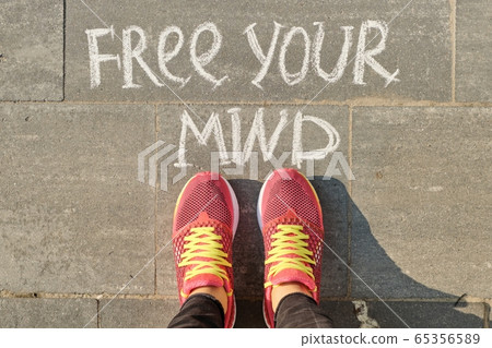 Free your mind text on gray sidewalk with woman legs in sneakers, top view 65356589