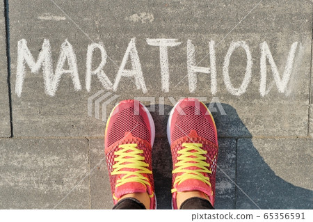 Marathon written on gray sidewalk with woman legs in sneakers, top view 65356591
