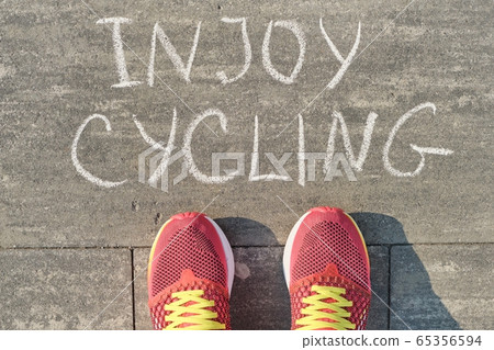 Enjoy cycling, text on gray sidewalk with woman legs in sneakers, top view 65356594
