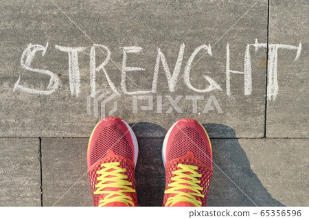 Strength, written on gray sidewalk with woman legs in sneakers, top view 65356596