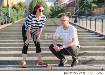 Mature couple in city near the stairs, middle-aged man and woman in sportswear talking resting after running Mature couple in city near the stairs, middle-aged man and woman in sportswear talking resting after running 65356597