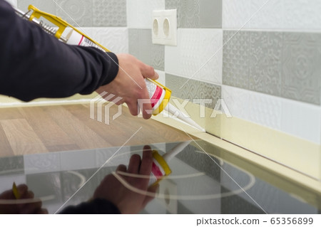 Applying silicone sealant with construction syringe. Worker fills seam between the ceramic tiles on the wall and kitchen worktop Applying silicone sealant with construction syringe. Worker fills seam between the ceramic tiles on the wall and kitchen worktop 65356899