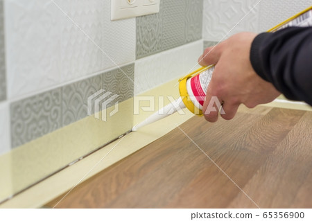 Applying silicone sealant with construction syringe. Worker fills seam between the ceramic tiles on the wall and kitchen worktop Applying silicone sealant with construction syringe. Worker fills seam between the ceramic tiles on the wall and kitchen worktop 65356900