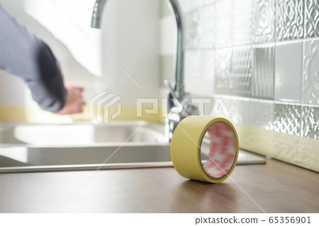 Worker protecting countertop in kitchen with masking tape before starting construction repairs with ceramic tiles Worker protecting countertop in kitchen with masking tape before starting construction repairs with ceramic tiles 65356901