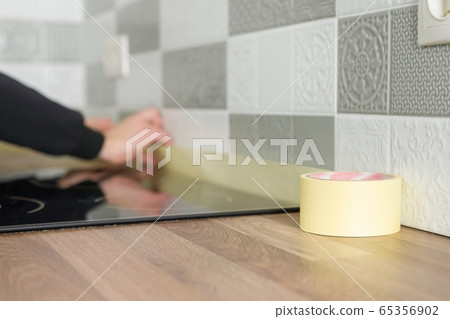Worker protecting countertop in kitchen with masking tape before starting construction repairs with ceramic tiles 65356902