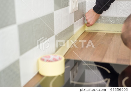Worker protecting countertop in kitchen with masking tape before starting construction repairs with ceramic tiles Worker protecting countertop in kitchen with masking tape before starting construction repairs with ceramic tiles 65356903