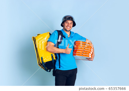 Contacless delivery service during quarantine. Man delivers food and shopping bags during insulation. Emotions of deliveryman isolated on blue background. Contacless delivery service during quarantine. Man delivers food and shopping bags during insulation. Emotions of deliveryman isolated on blue background. 65357666