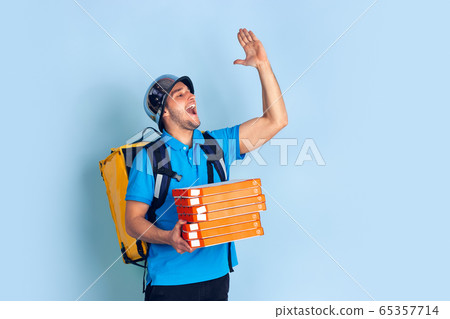 Contacless delivery service during quarantine. Man delivers food and shopping bags during insulation. Emotions of deliveryman isolated on blue background. Contacless delivery service during quarantine. Man delivers food and shopping bags during insulation. Emotions of deliveryman isolated on blue background. 65357714