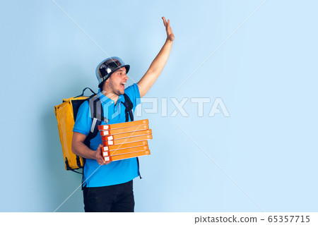 Contacless delivery service during quarantine. Man delivers food and shopping bags during insulation. Emotions of deliveryman isolated on blue background. Contacless delivery service during quarantine. Man delivers food and shopping bags during insulation. Emotions of deliveryman isolated on blue background. 65357715