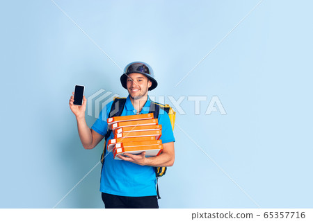 Contacless delivery service during quarantine. Man delivers food and shopping bags during insulation. Emotions of deliveryman isolated on blue background. 65357716
