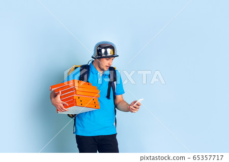 Contacless delivery service during quarantine. Man delivers food and shopping bags during insulation. Emotions of deliveryman isolated on blue background. Contacless delivery service during quarantine. Man delivers food and shopping bags during insulation. Emotions of deliveryman isolated on blue background. 65357717