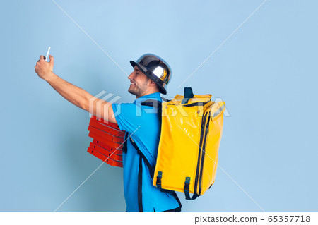 Contacless delivery service during quarantine. Man delivers food and shopping bags during insulation. Emotions of deliveryman isolated on blue background. Contacless delivery service during quarantine. Man delivers food and shopping bags during insulation. Emotions of deliveryman isolated on blue background. 65357718