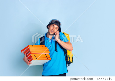 Contacless delivery service during quarantine. Man delivers food and shopping bags during insulation. Emotions of deliveryman isolated on blue background. Contacless delivery service during quarantine. Man delivers food and shopping bags during insulation. Emotions of deliveryman isolated on blue background. 65357719