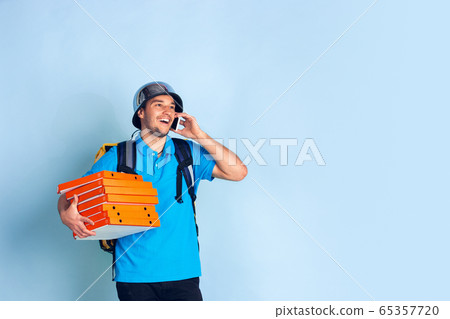 Contacless delivery service during quarantine. Man delivers food and shopping bags during insulation. Emotions of deliveryman isolated on blue background. Contacless delivery service during quarantine. Man delivers food and shopping bags during insulation. Emotions of deliveryman isolated on blue background. 65357720
